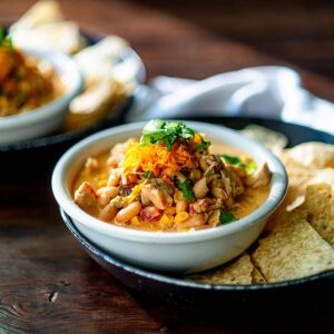 Instant Pot White Chicken Chili served in a white bowl topped with cheese and cilantro served with tortilla chips.