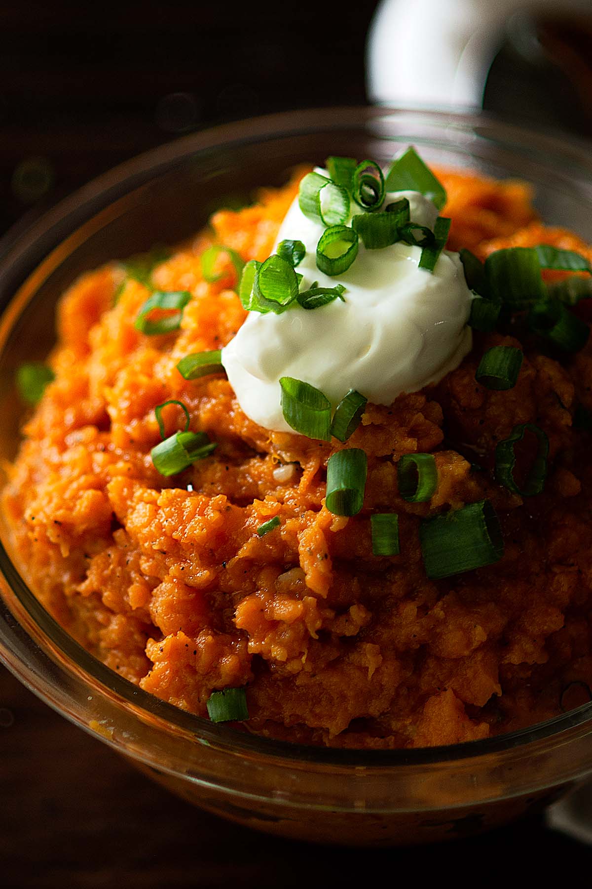 Mashed sweet potatoes in a serving dish topped with sour cream and sliced green onions.