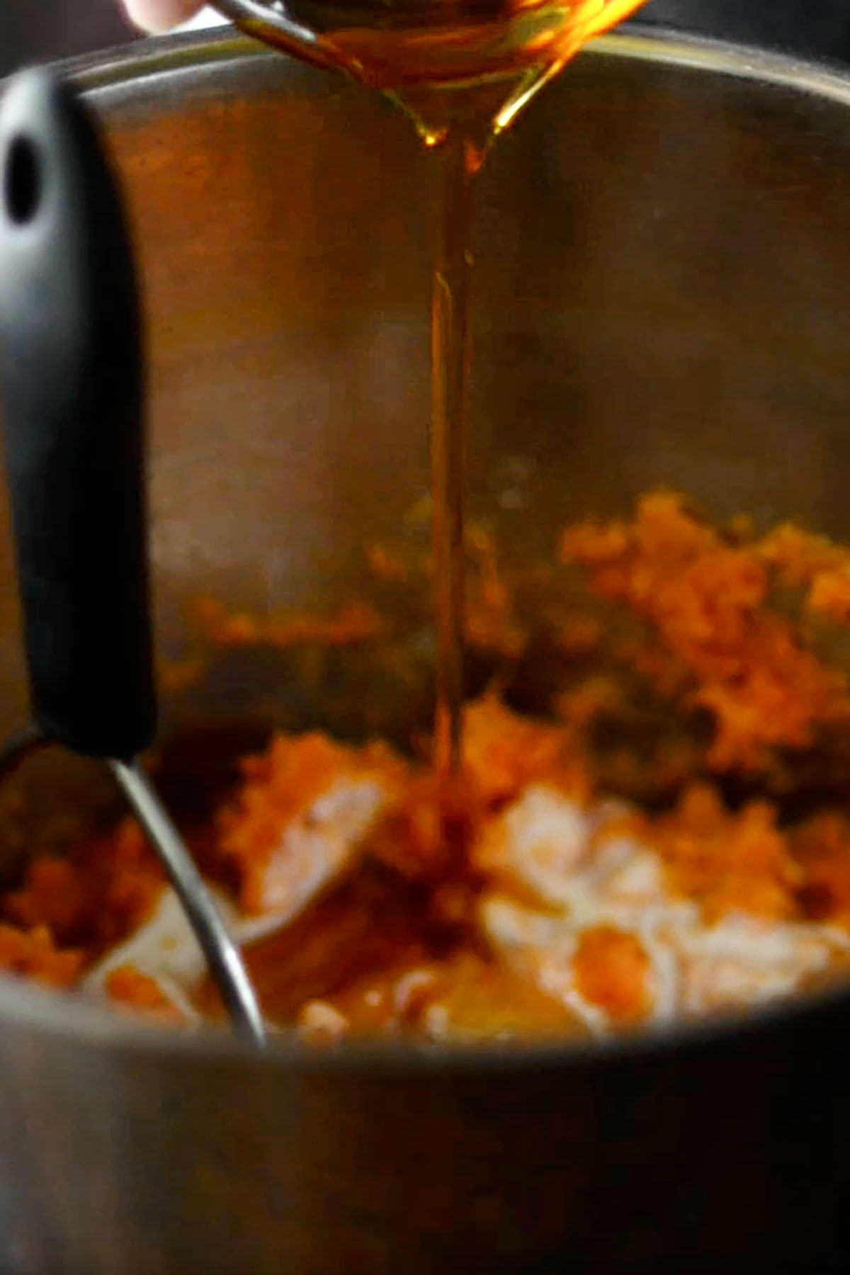Maple syrup being added to a pot of mashed sweet potatoes.