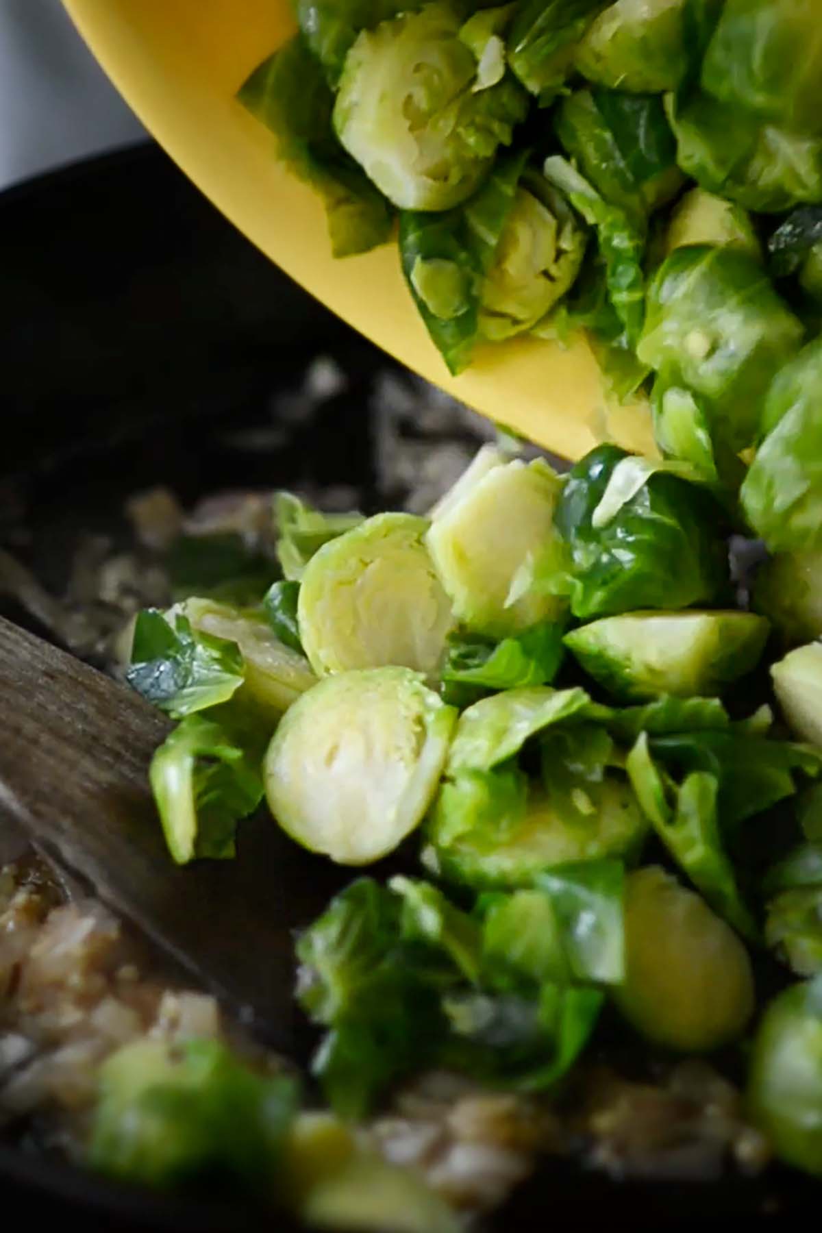Brussels sprouts being added to a cast iron skillet.