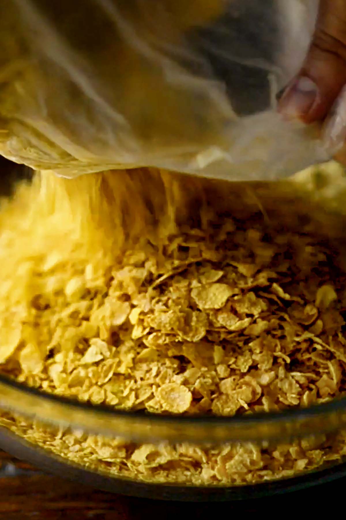 Corn flakes being poured into a glass mixing bowl.