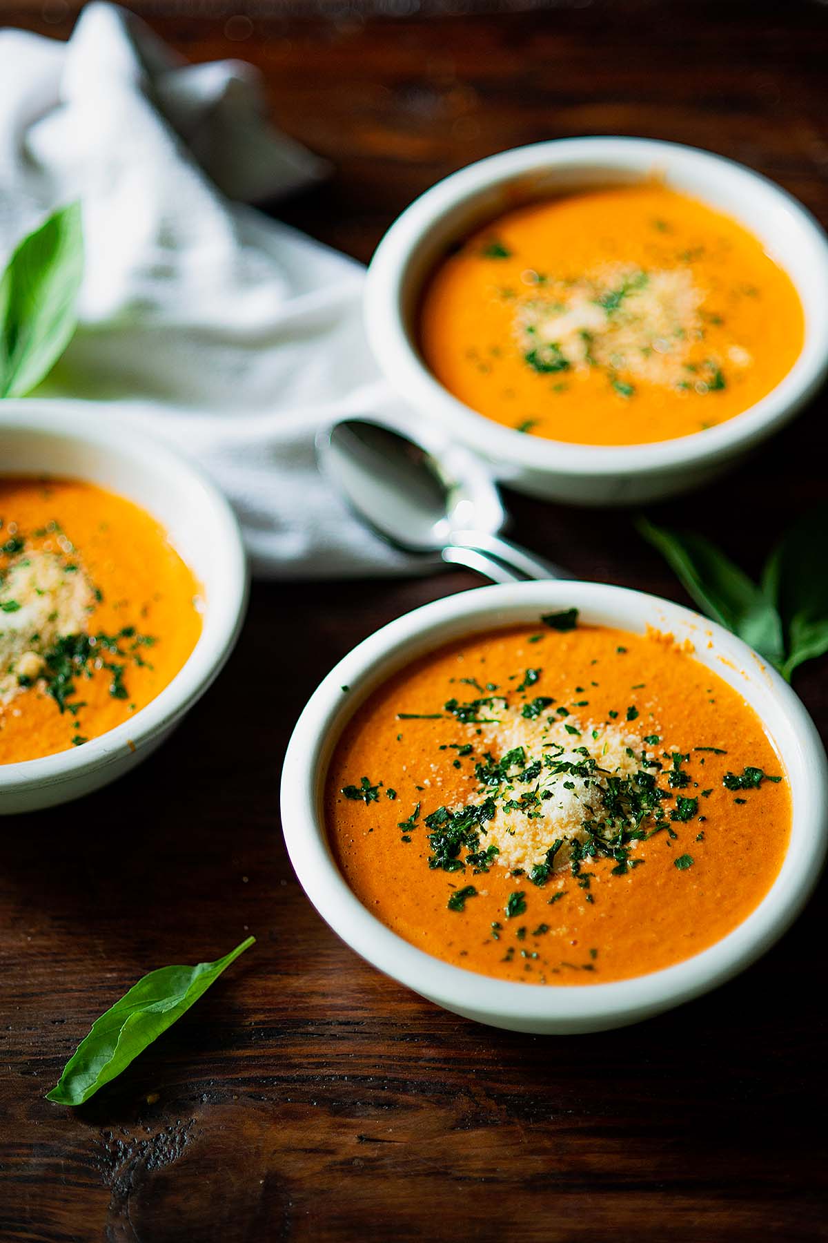 Three bowls of fresh tomato basil soup topped with parsley and parmesan cheese.