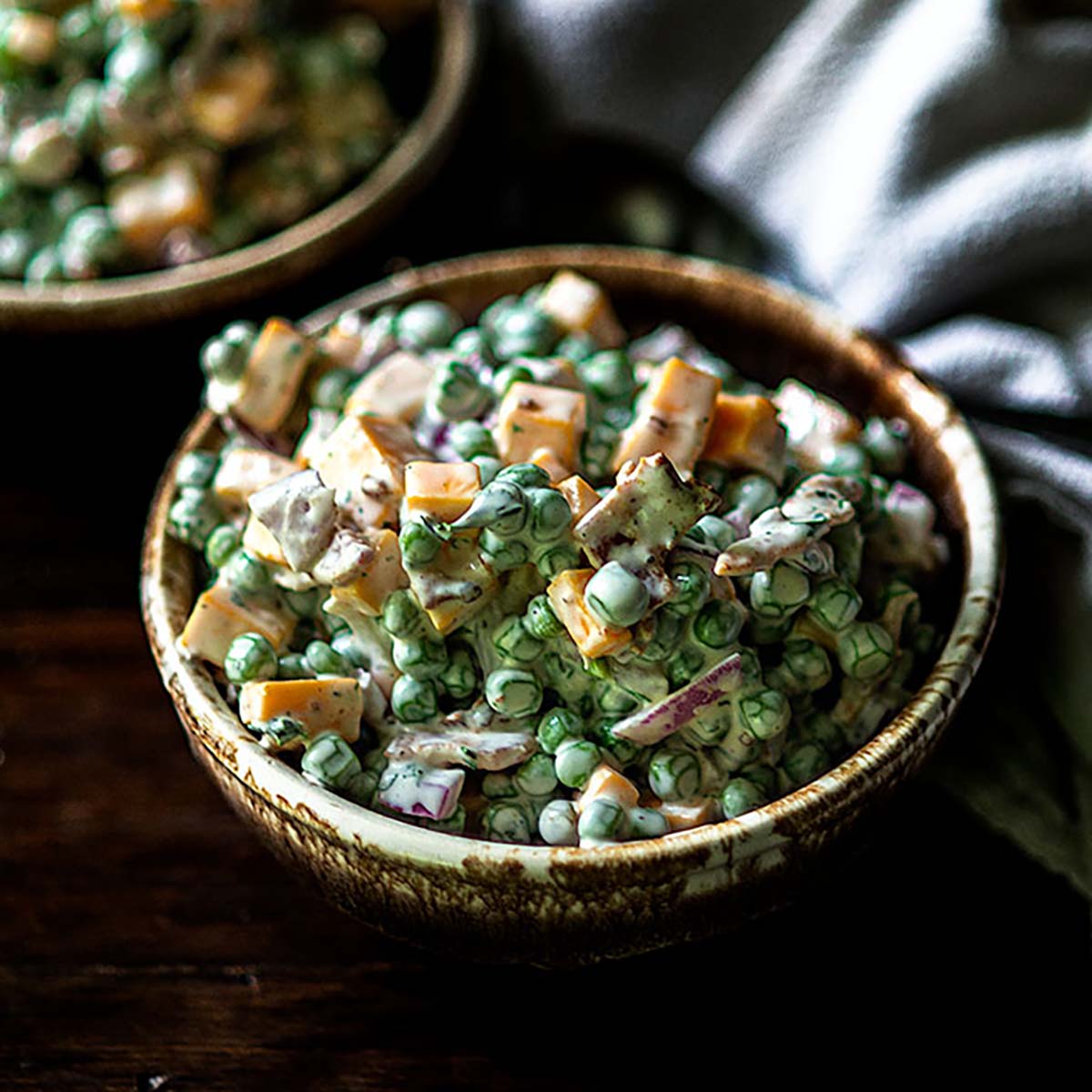 A rugged bowl on a wooden table filled with pea salad.