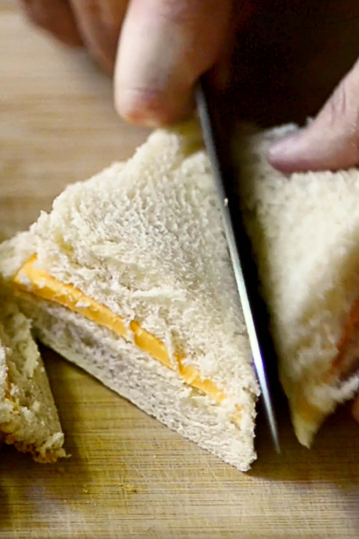 A cheese sandwich with the crust cut off being sliced in half diagonally.