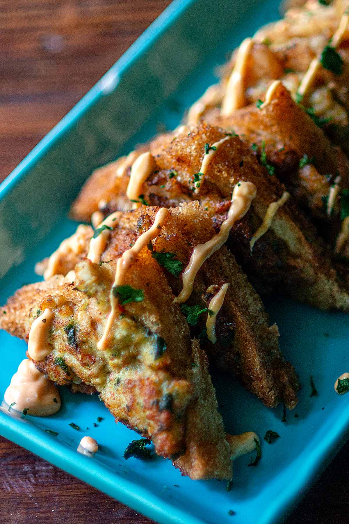 Shrimp toast served on a blue platter topped with spicy sauce.