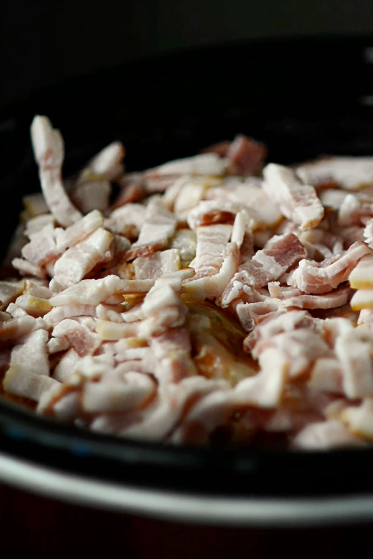 Sliced bacon covering the entire top of cabbage rolls in a crock pot.