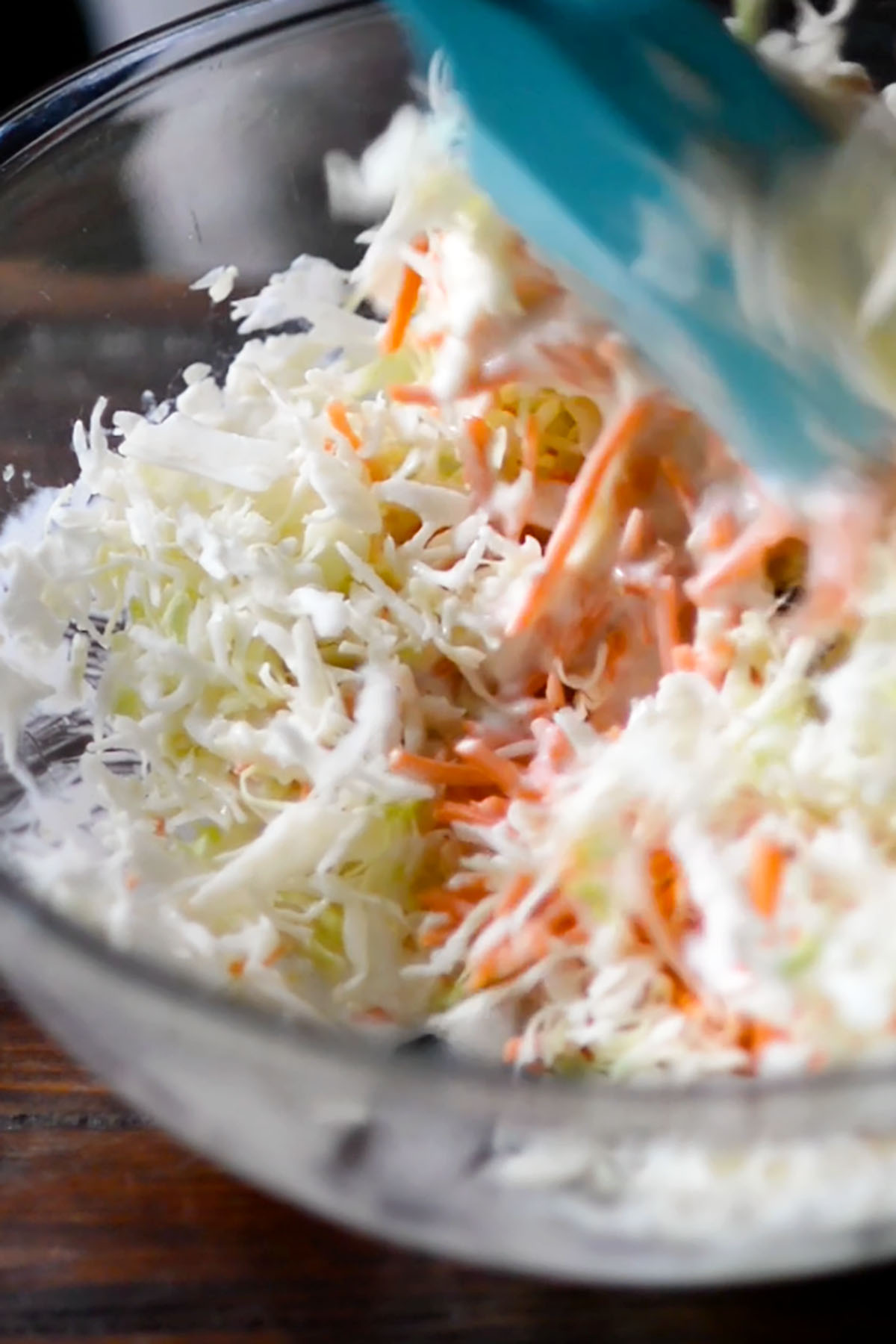 Coleslaw being tossed in a glass bowl.