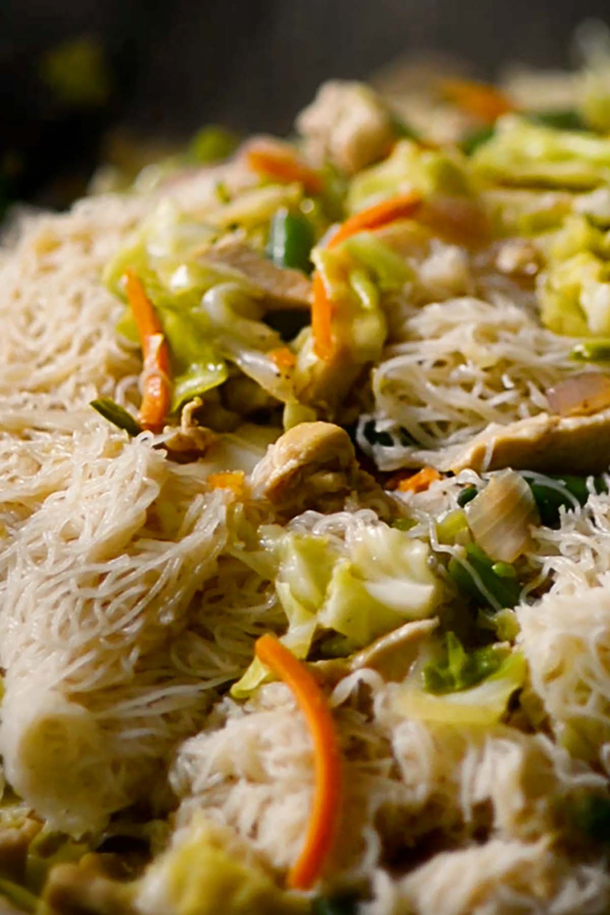 Rice Vermicelli noddles added to vegetable and chicken mixture in a hot wok.