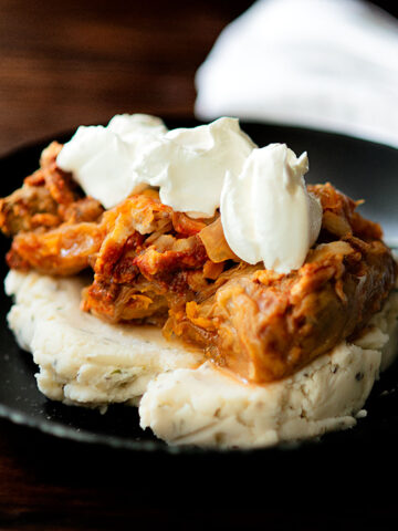 Sarmale served over a bed of mashed potatoes and topped with sour cream.