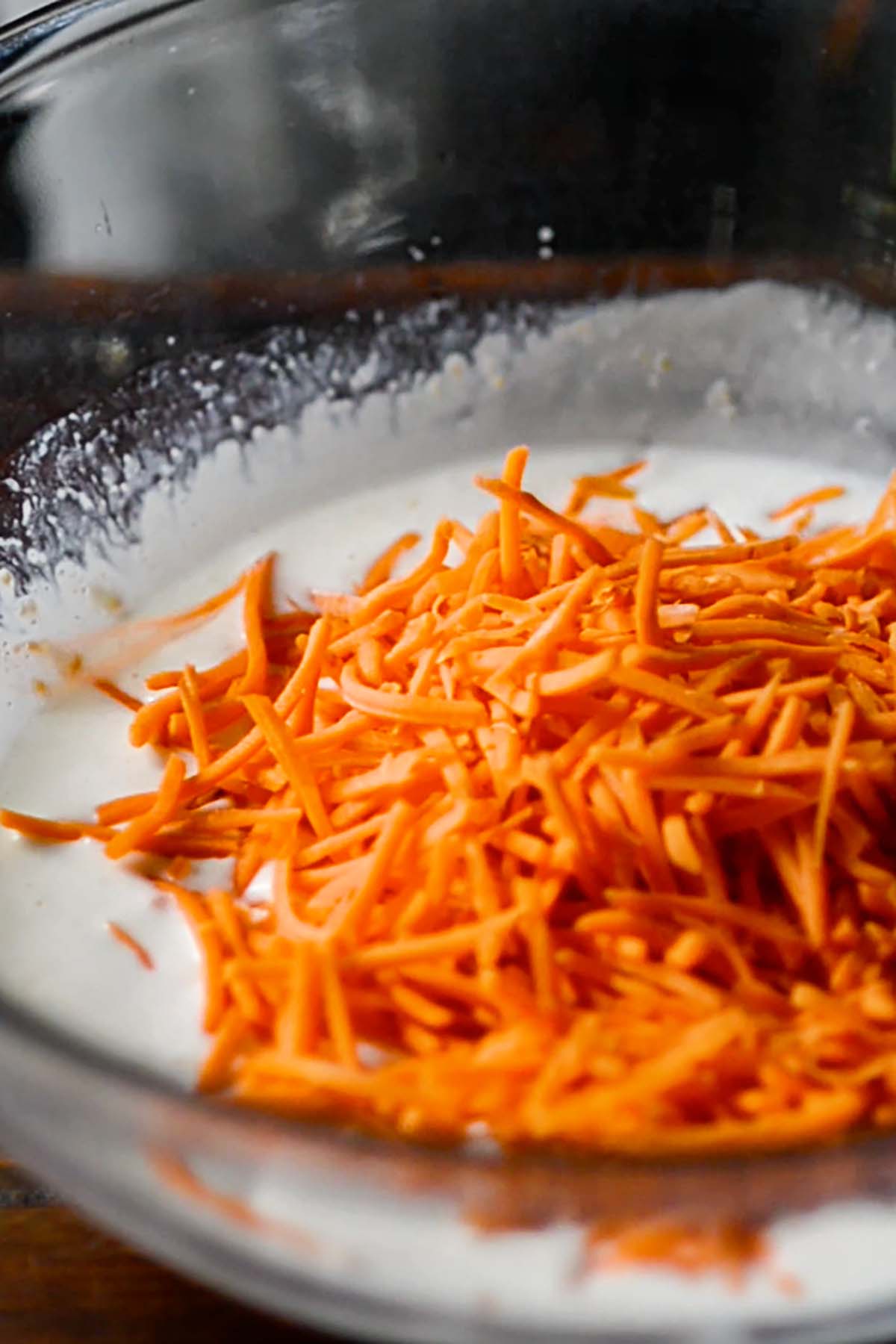 Carrots added to a creamy dressing in a glass missing bowl.