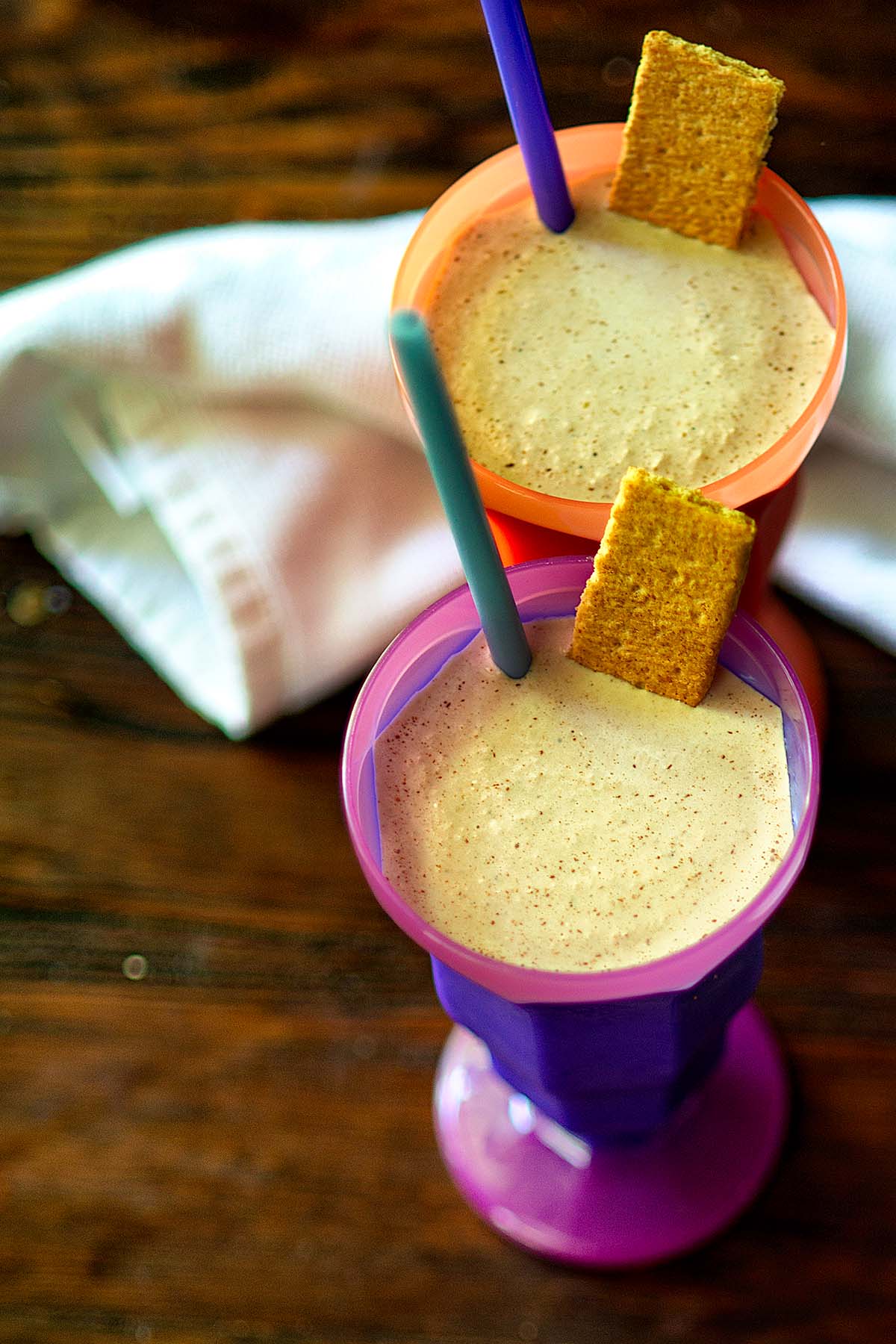 Two S'mores Malted Milkshakes served in colorful cups and garnished with graham cracker squares.