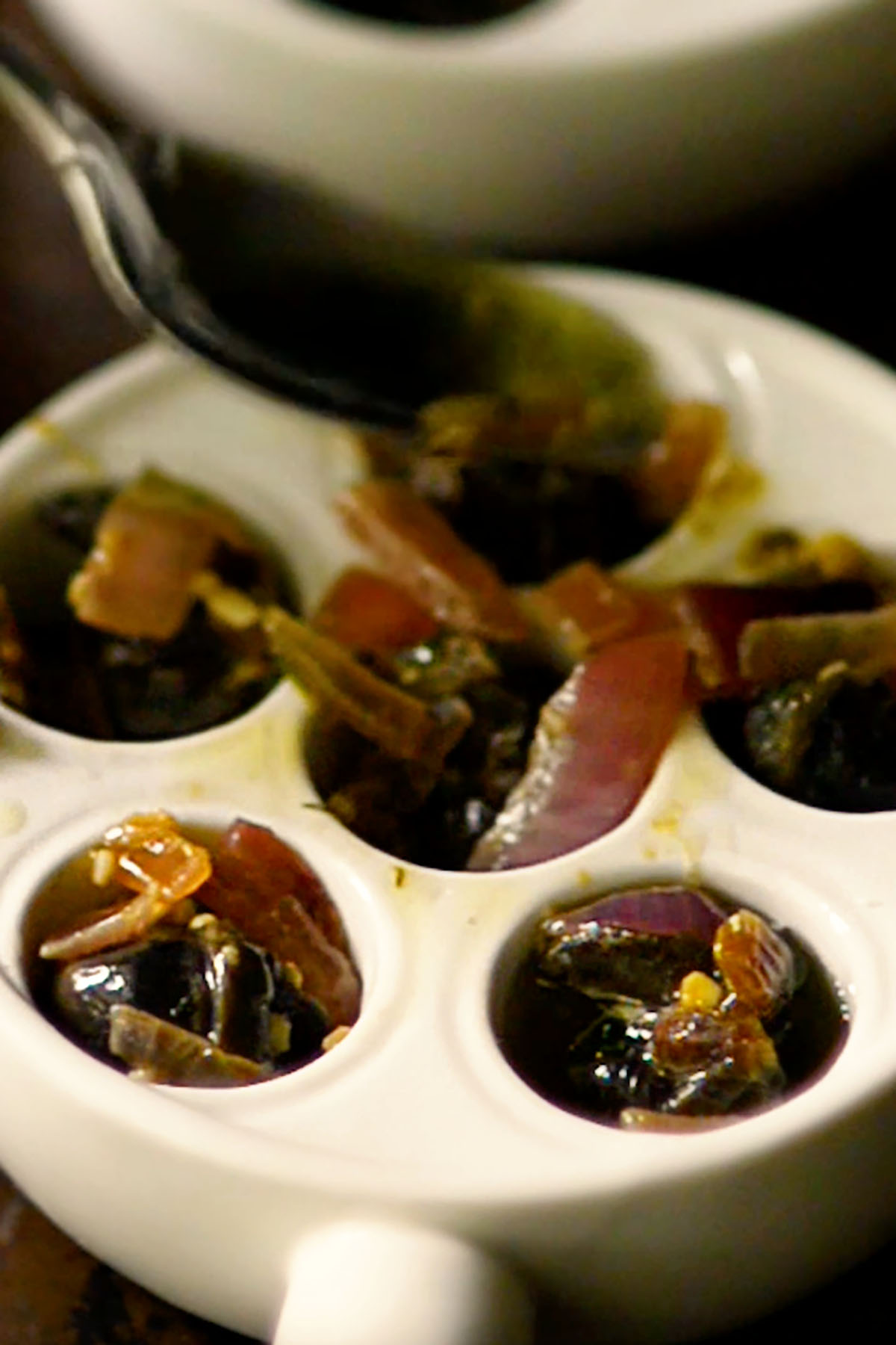 Snails, onions, and butter sauce added to escargot baking dishes.