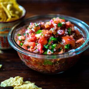 Pico de Gallo served in a glass bowl with tortilla chips on the side.