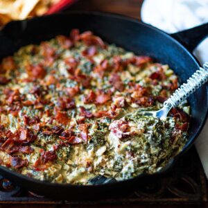 Asiago Kale Dip topped with crispy Bacon and served warm in a cast Iron skillet.