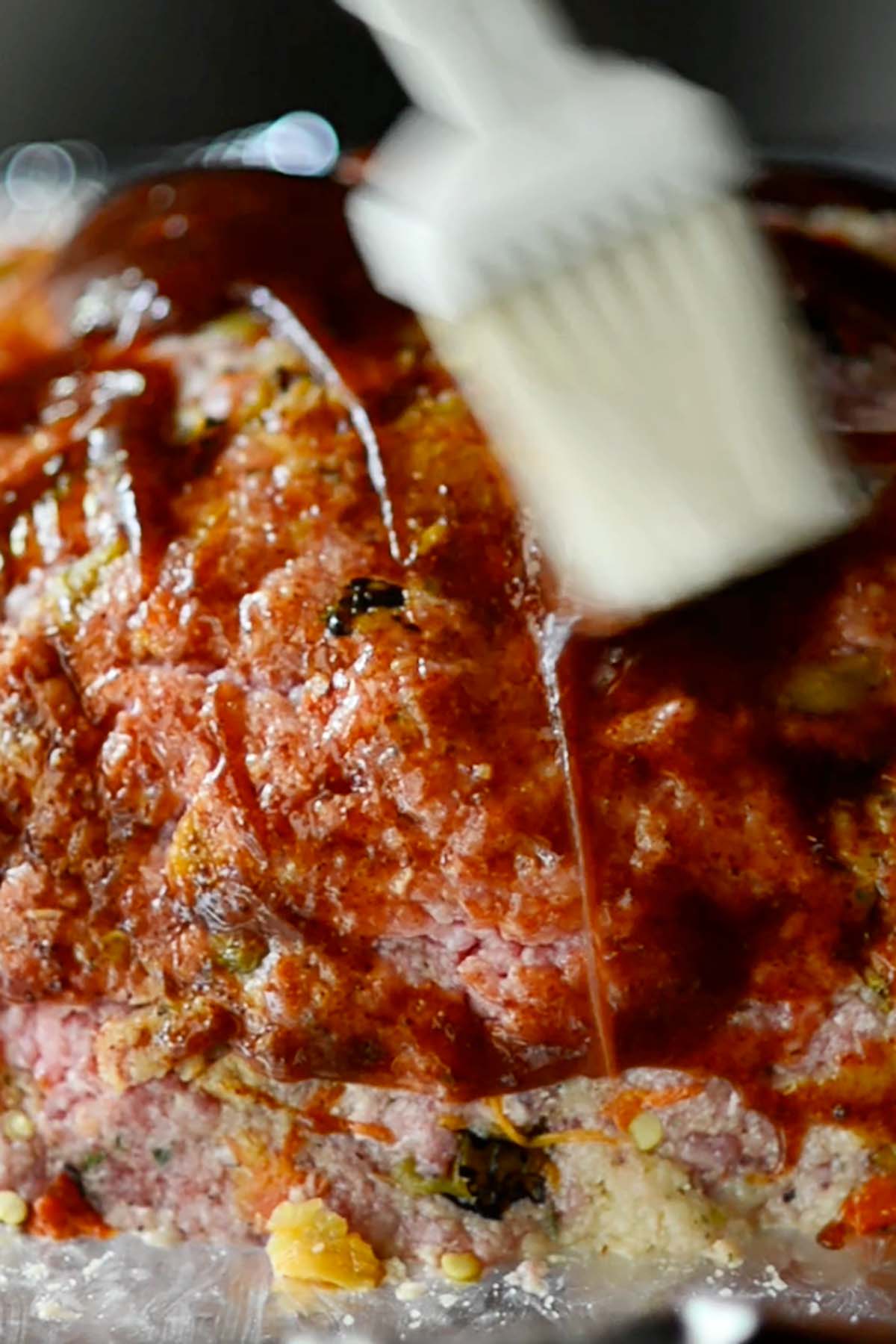 Ketchup based glaze being brushed over the top of meatloaf.