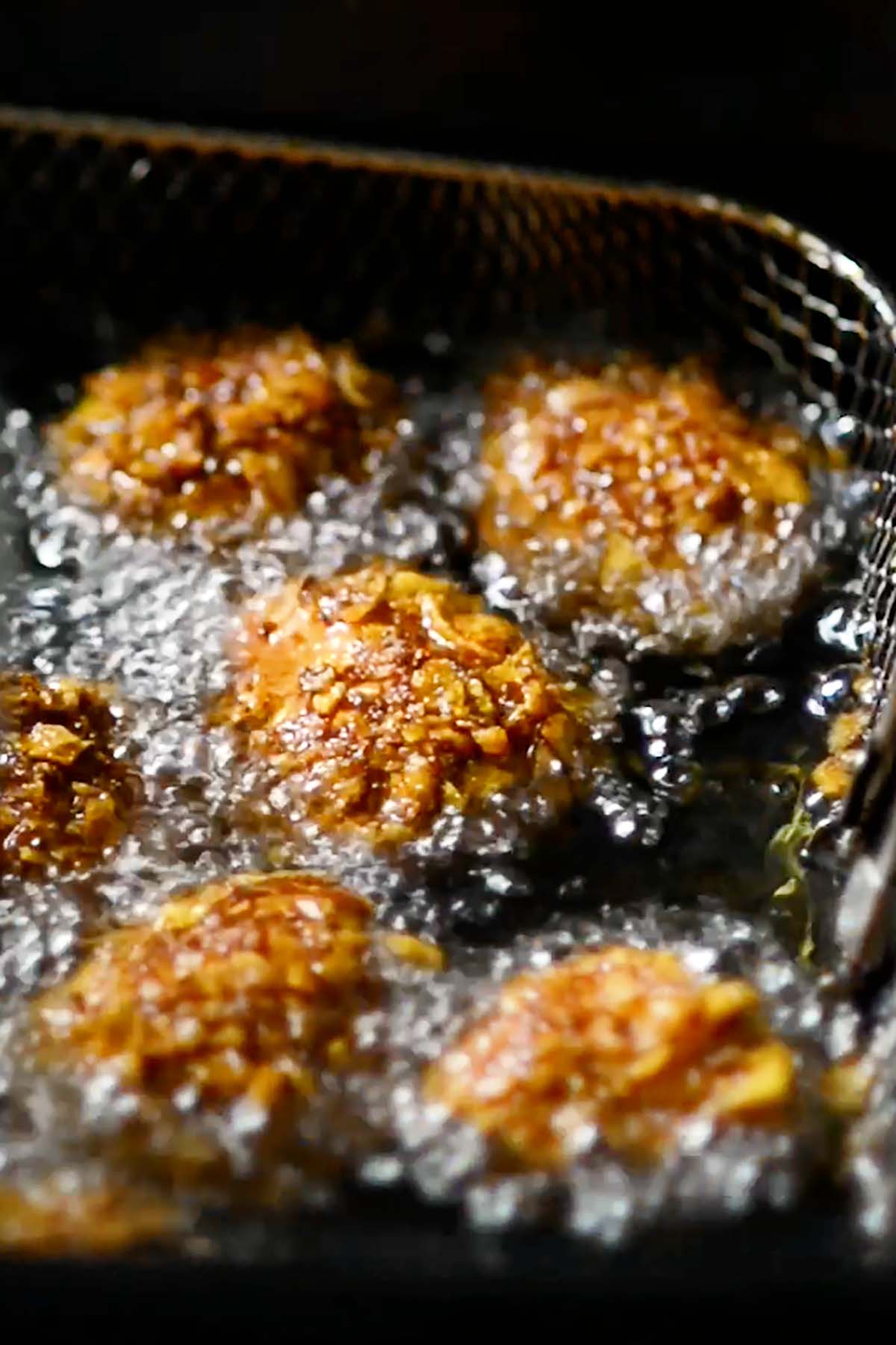 Frosted flake covered cheesecake balls deep frying in a fryer.