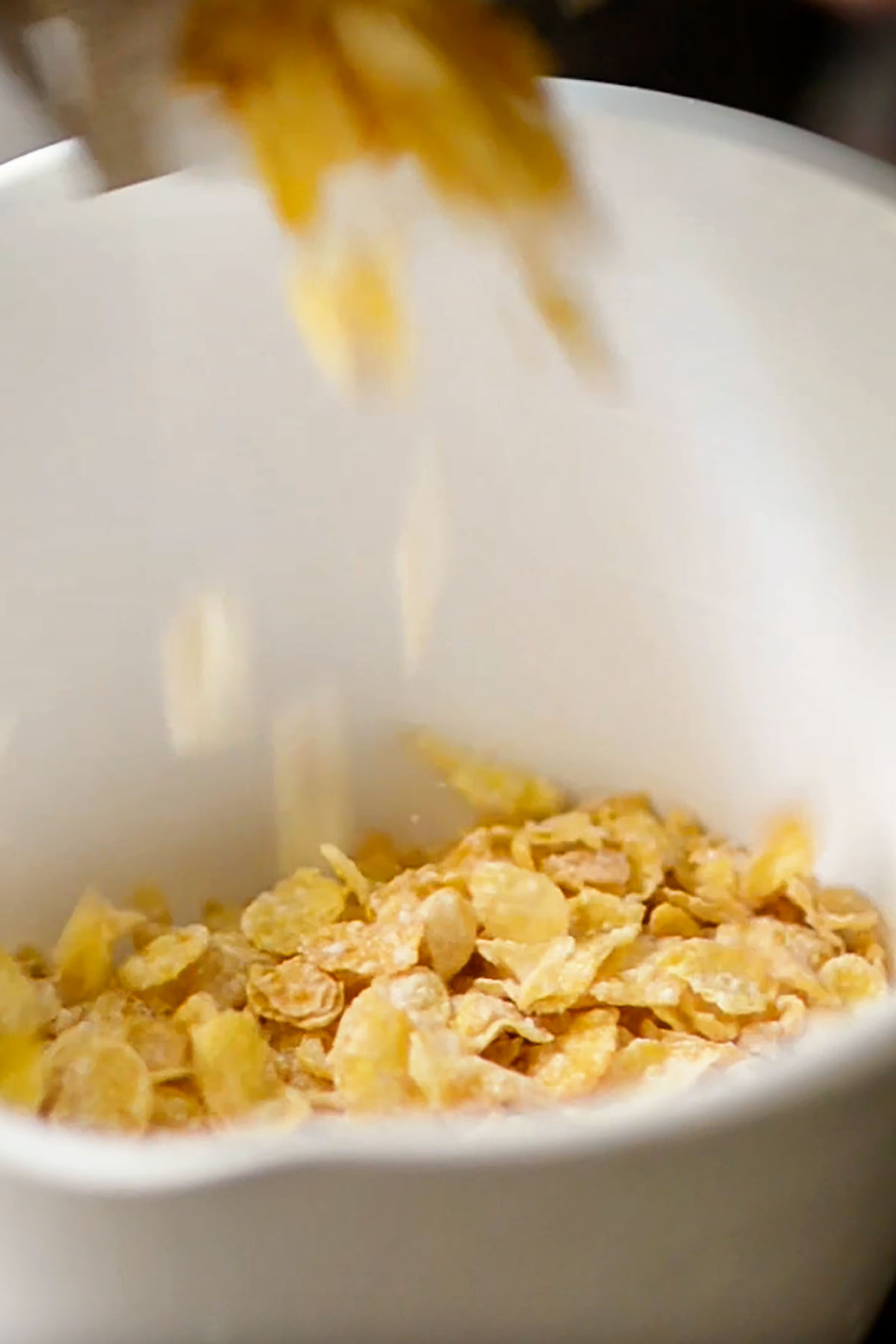 Frosted flakes being dumped in a white mixing bowl.