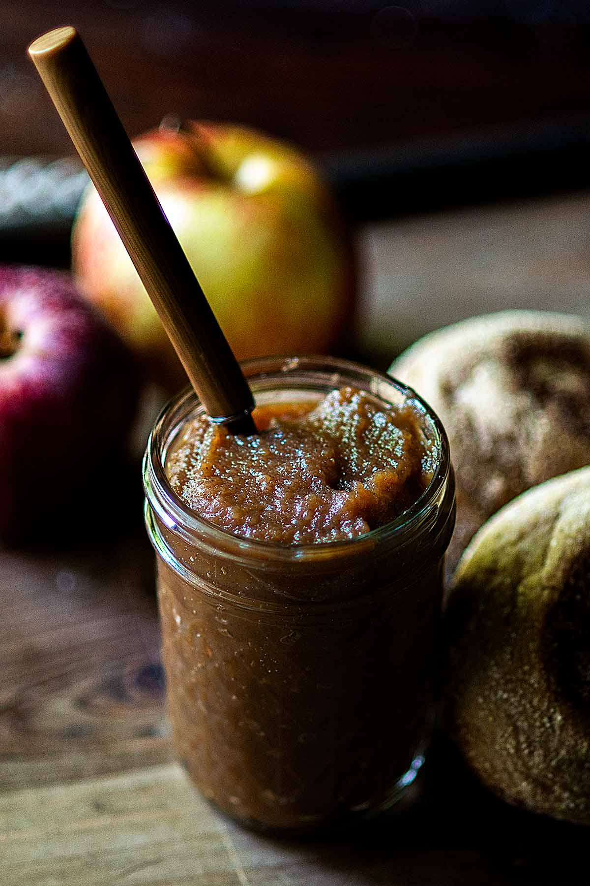 Apple butter in a jar with a spoon and english muffins.