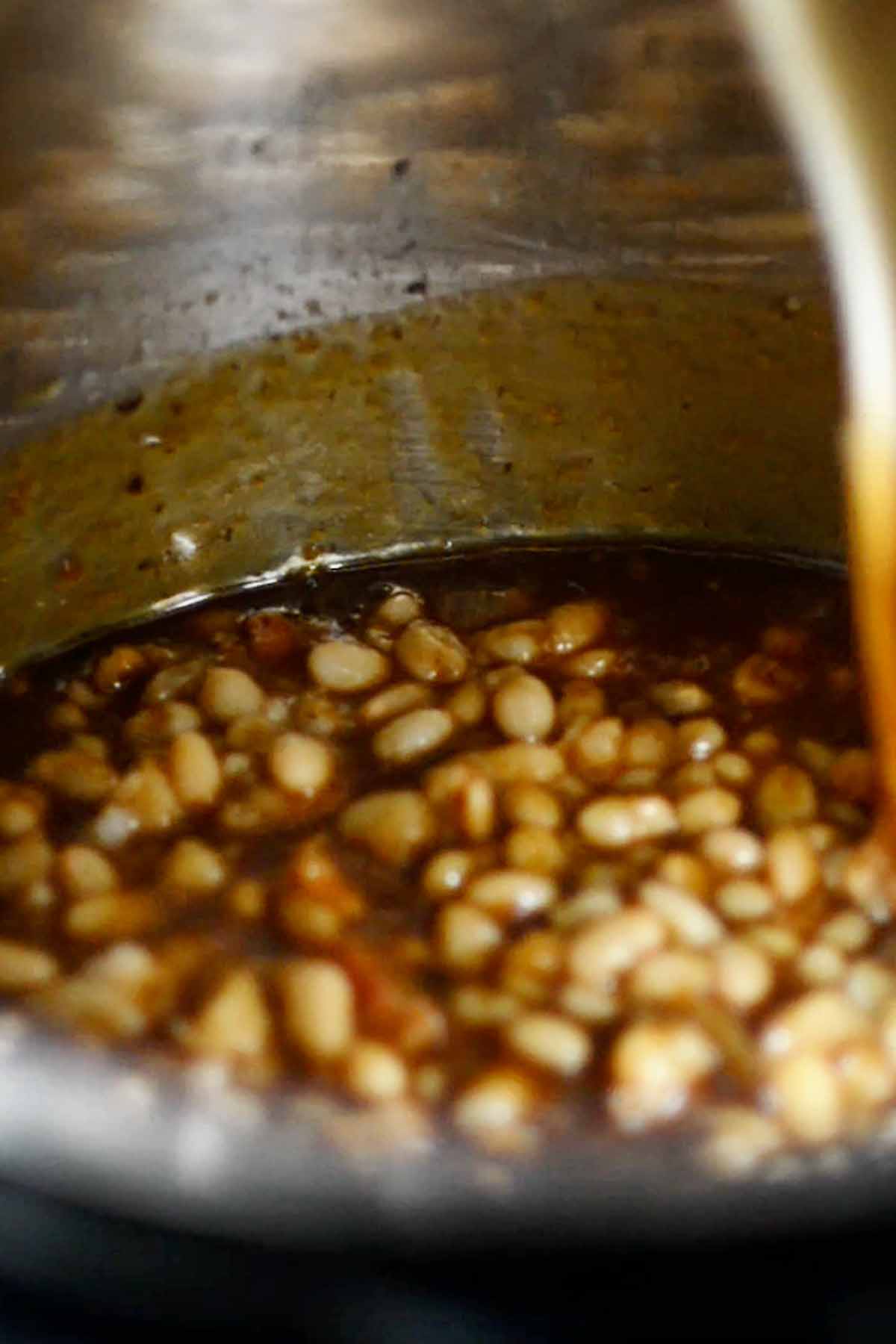 Baked beans being stirred in an Instant pot before being fully cooked.