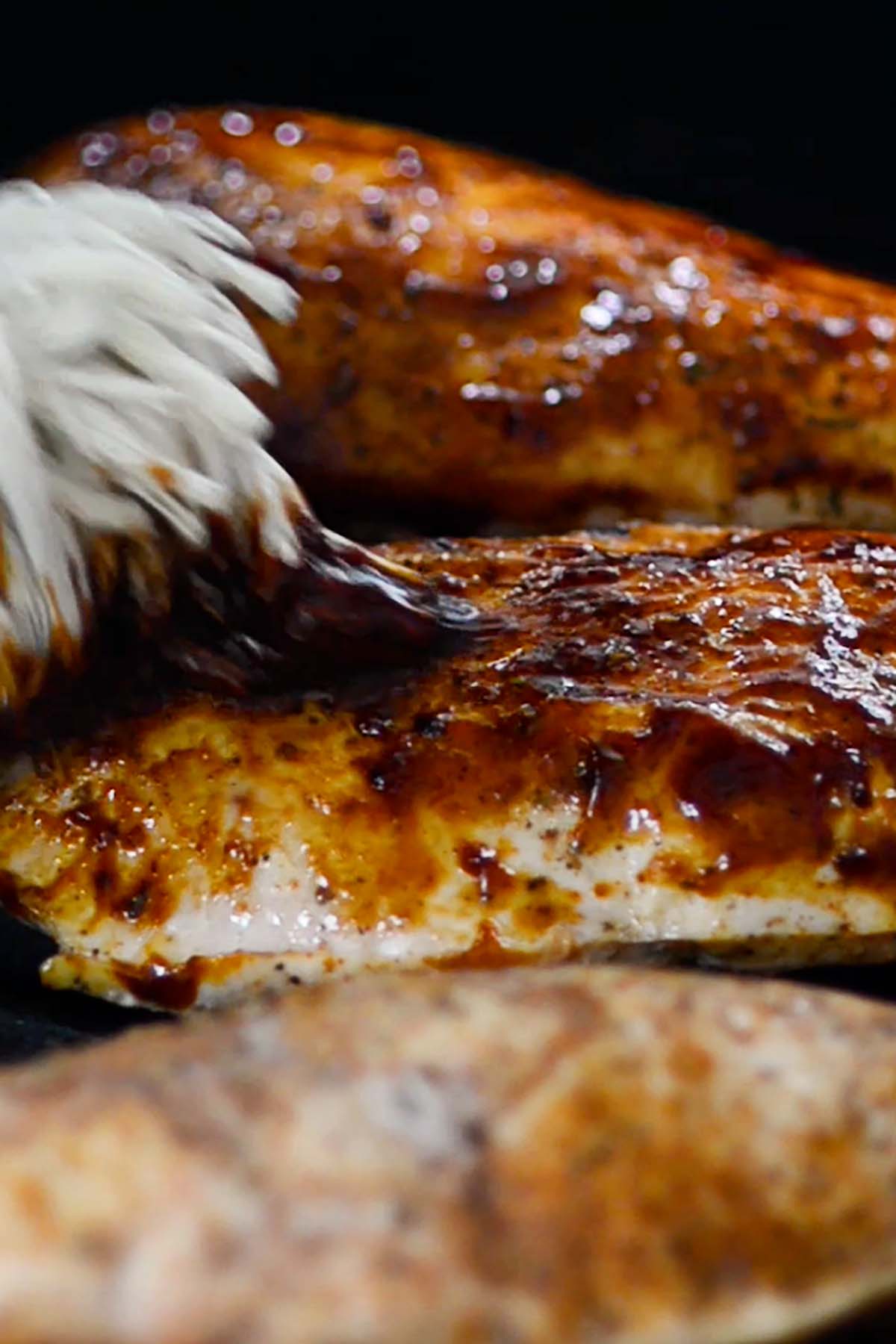 BBQ Sauce being brushed over grilled chicken breasts.
