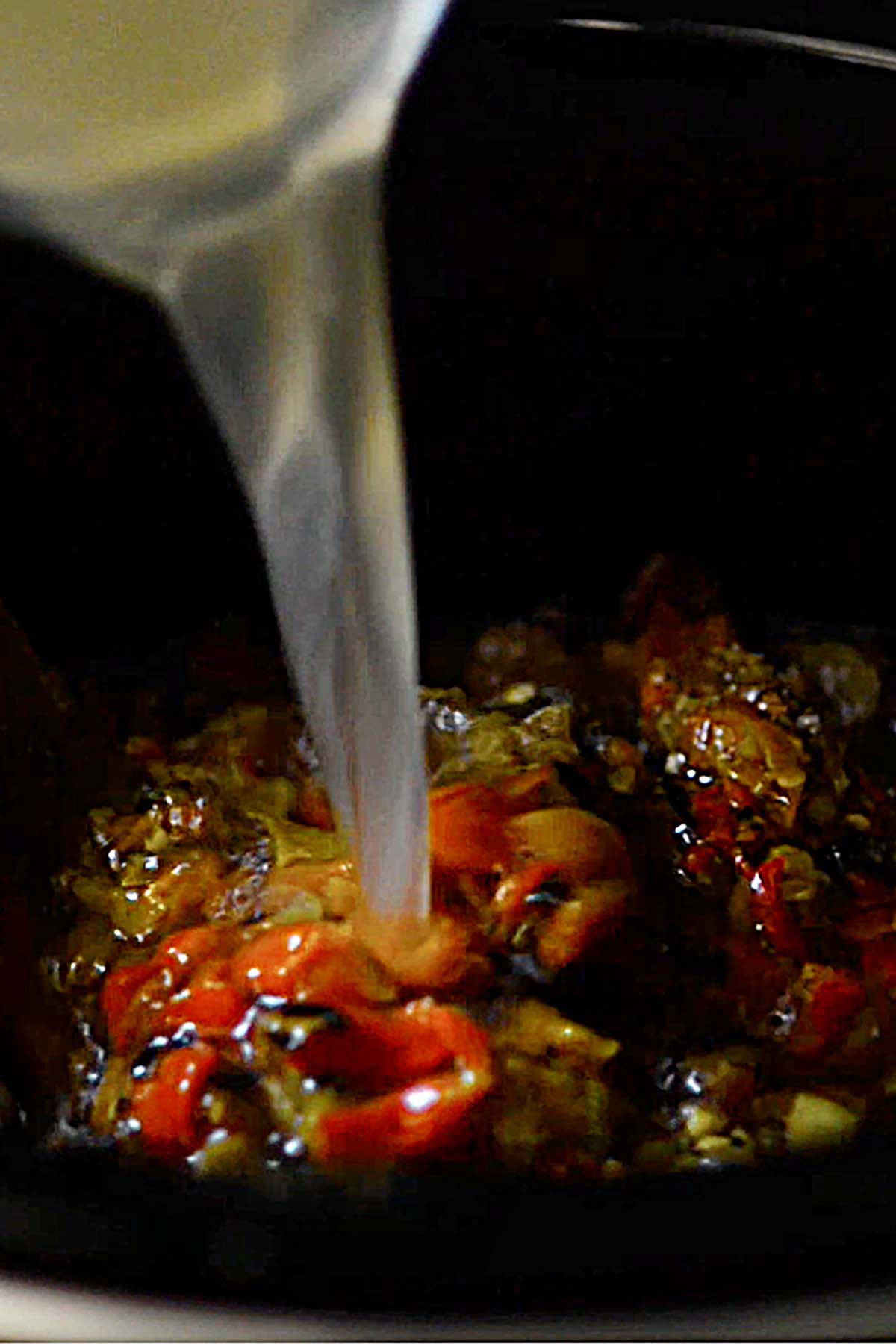 Chicken broth being poured into a slow cooker with diced roasted hatch chiles.