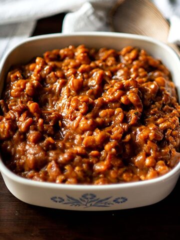 Instant Pot Baked Beans served in a vintage baking dish with a wooden serving spoon.