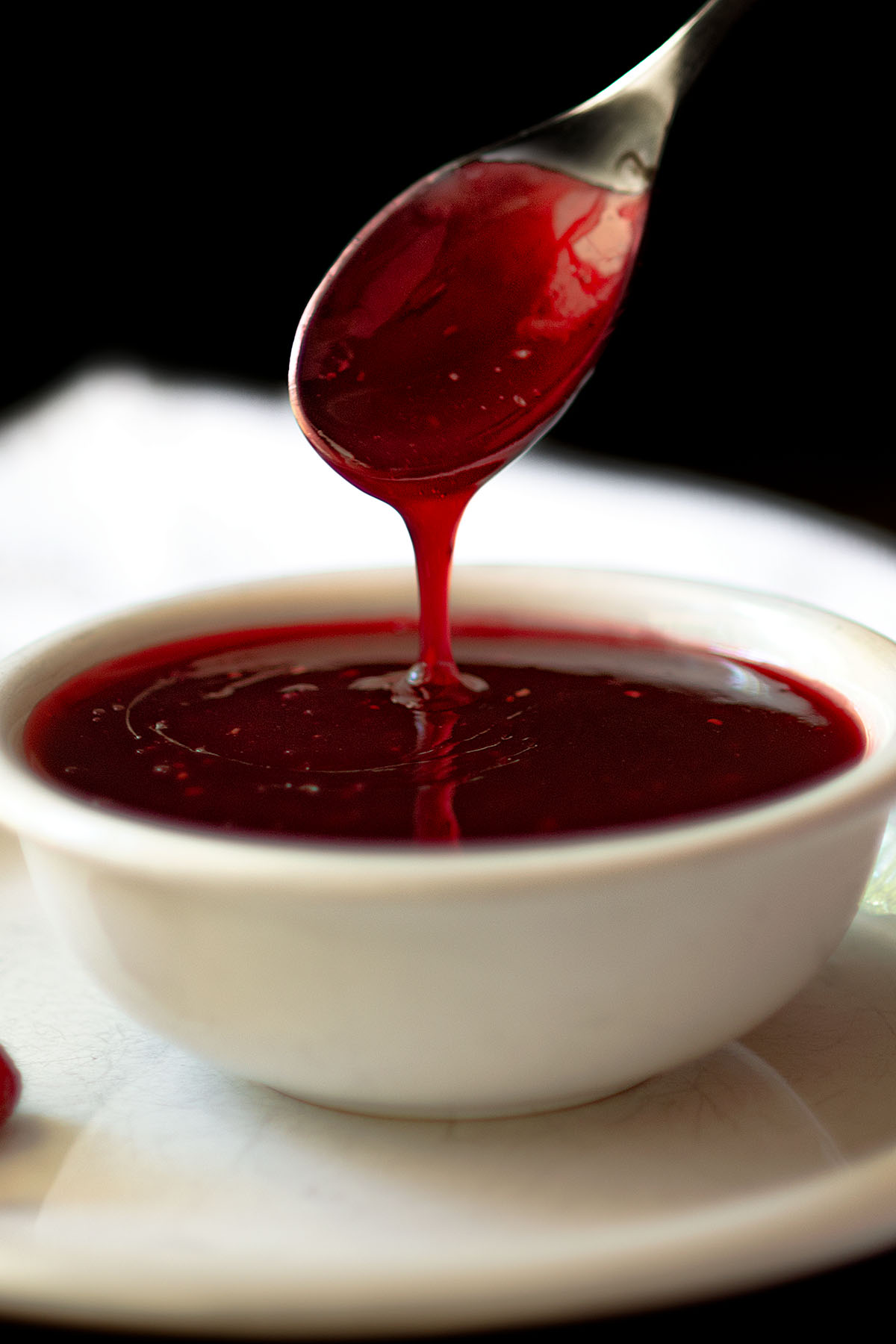 A bowl or raspberry dipping sauce with a spoon dripping sauce.