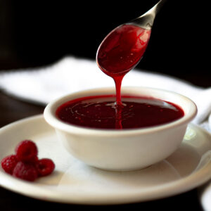A spoon dripping raspberry dipping sauce back into the bowl.