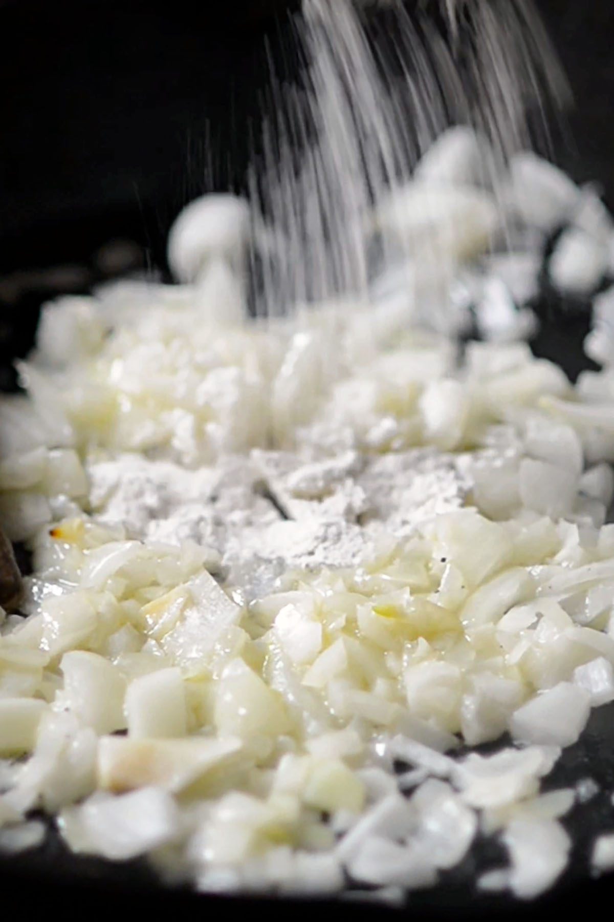 Flour being added to onions in a cast iron skillet.