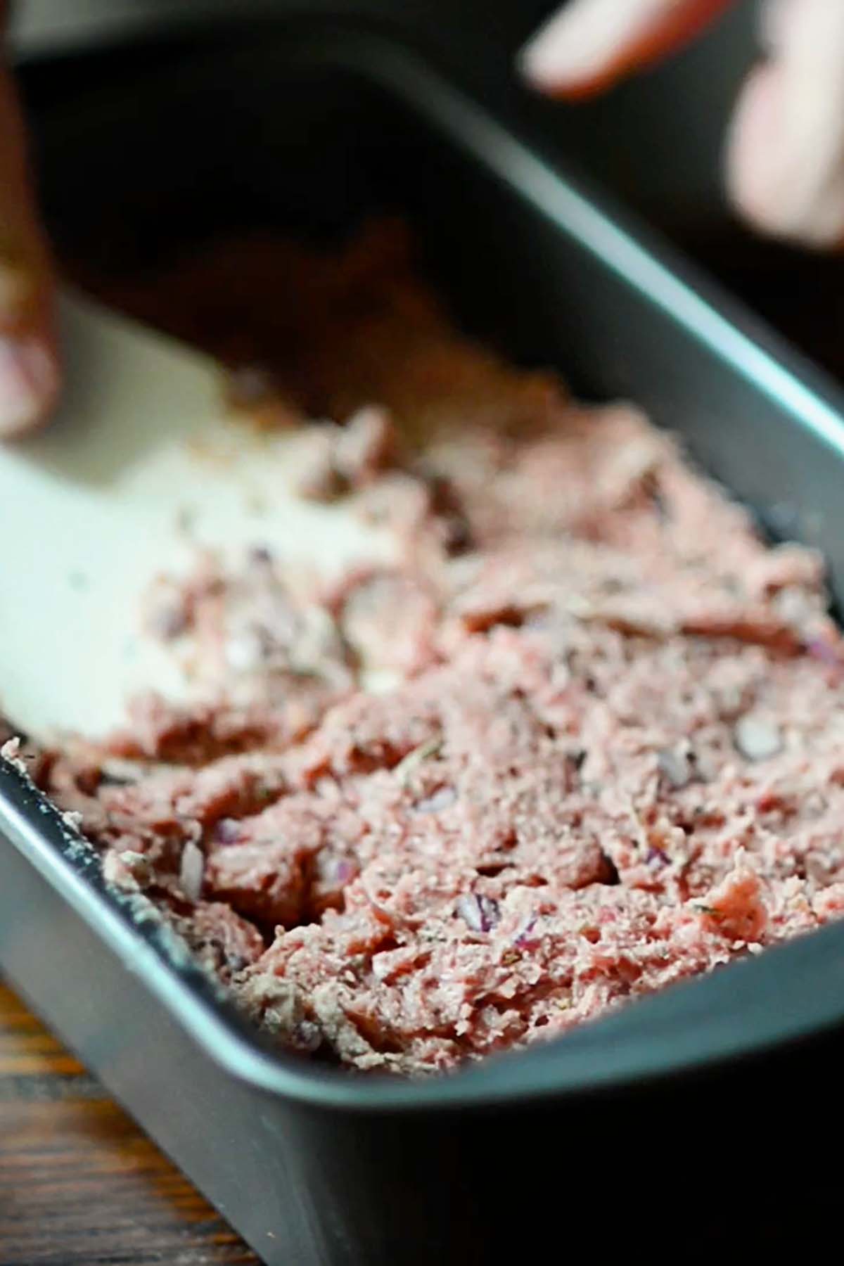 Homemade gyro meat being pressed tightly into a loaf pan.
