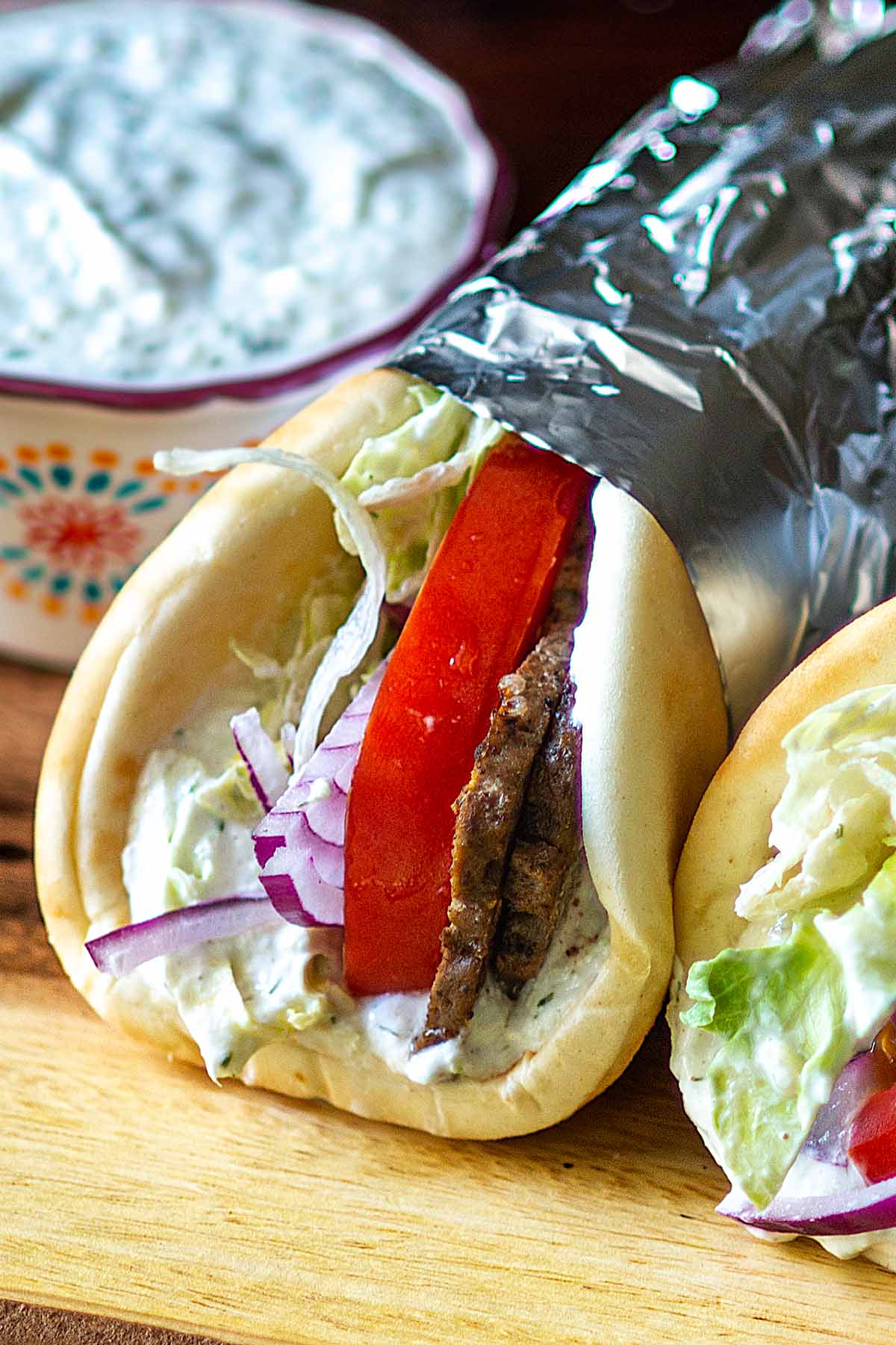 Homemade Gyros wrapped in foil and served on a wooden serving board.