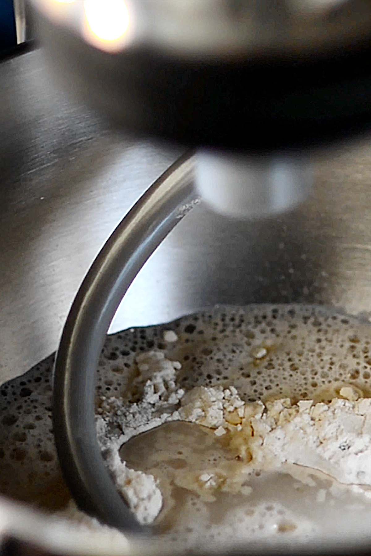 A dough hook on a stand mixer in a bowl of rosemary bread flour mix with water and yeast.