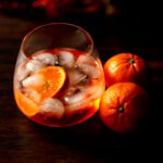 A stemless wine glass of aperol spritz with two oranges next to it.
