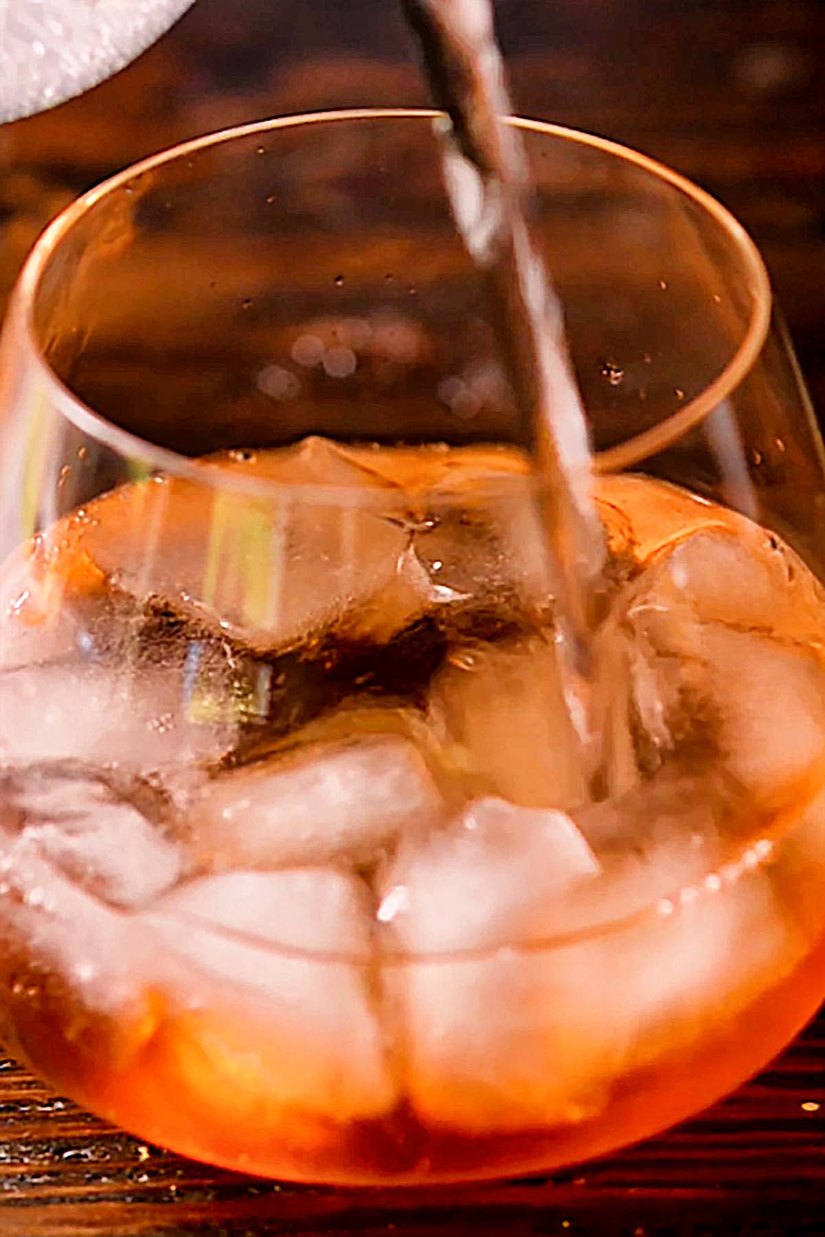 A splash of Tonic Water being added to a wine glass of Ice, Prosecco, and Aperol.