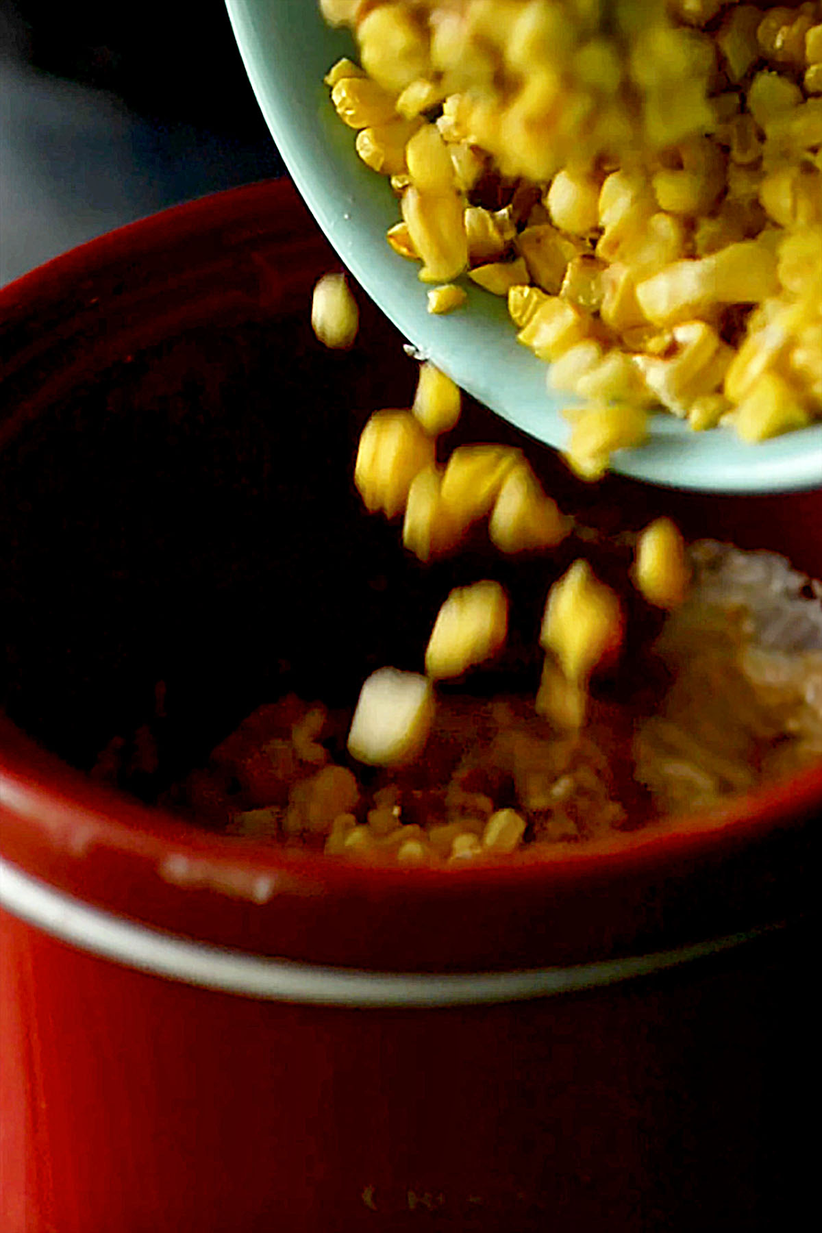 Roasted corn kernels being poured into a small slow cooker.