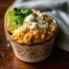 Elotes, Mexican-style street corn served in a cup, topped with Cotija Cheese, and garnished with a lime wedge and cilantro.