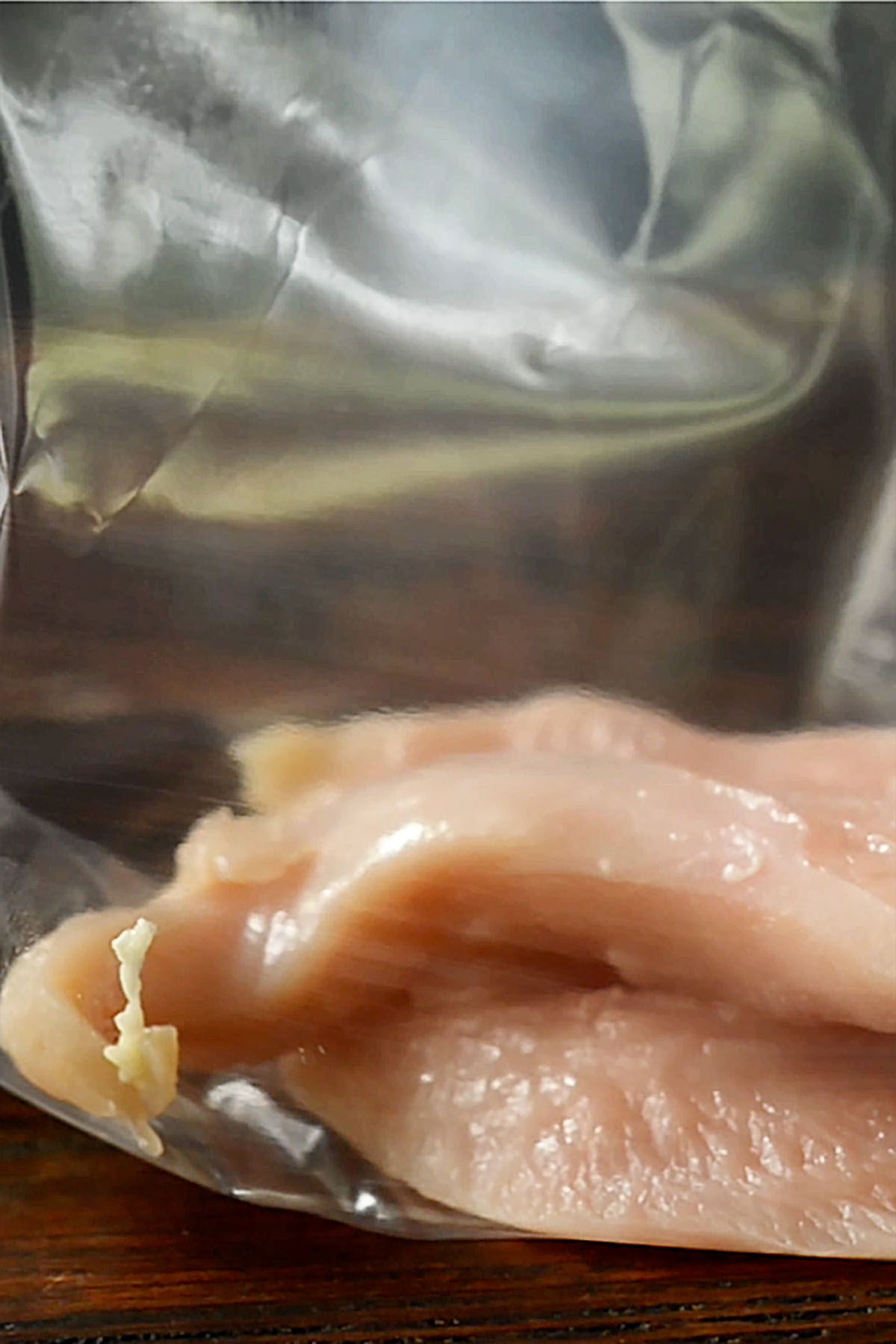 Halved chicken breast being added to a zip top bag.