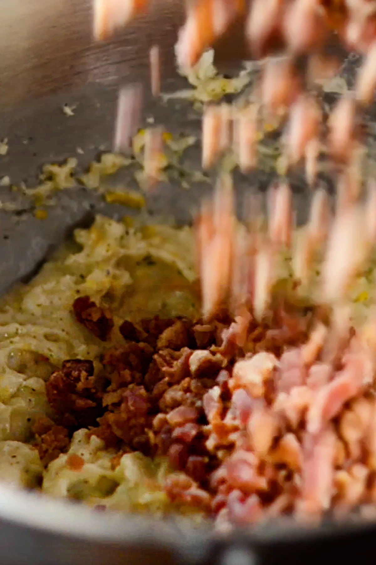 Bacon bits being added to mashed potatoes in a mixing bowl.
