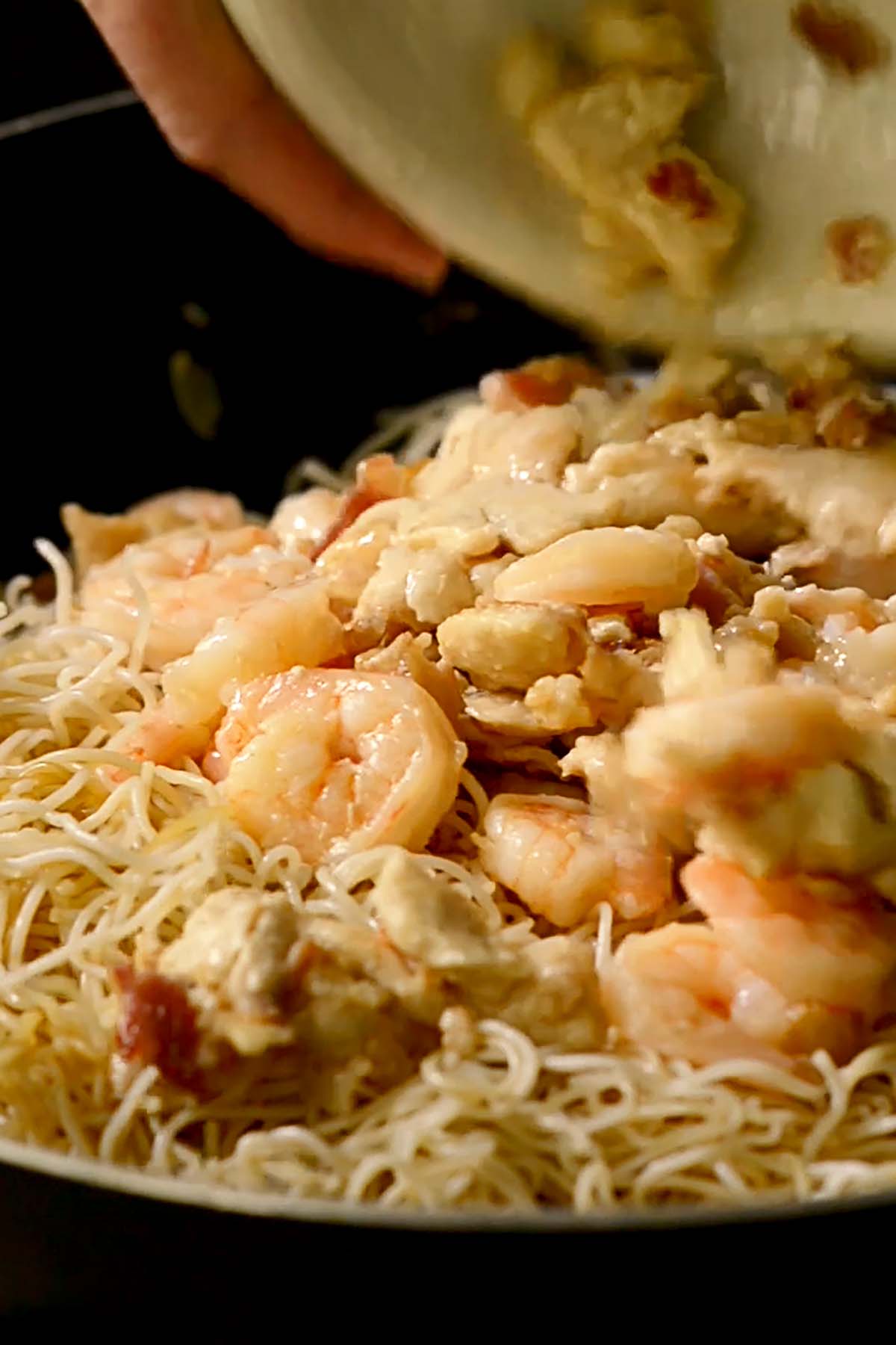 Cooked chicken, shrimp, and bacon added to vermicelli in a large wok.