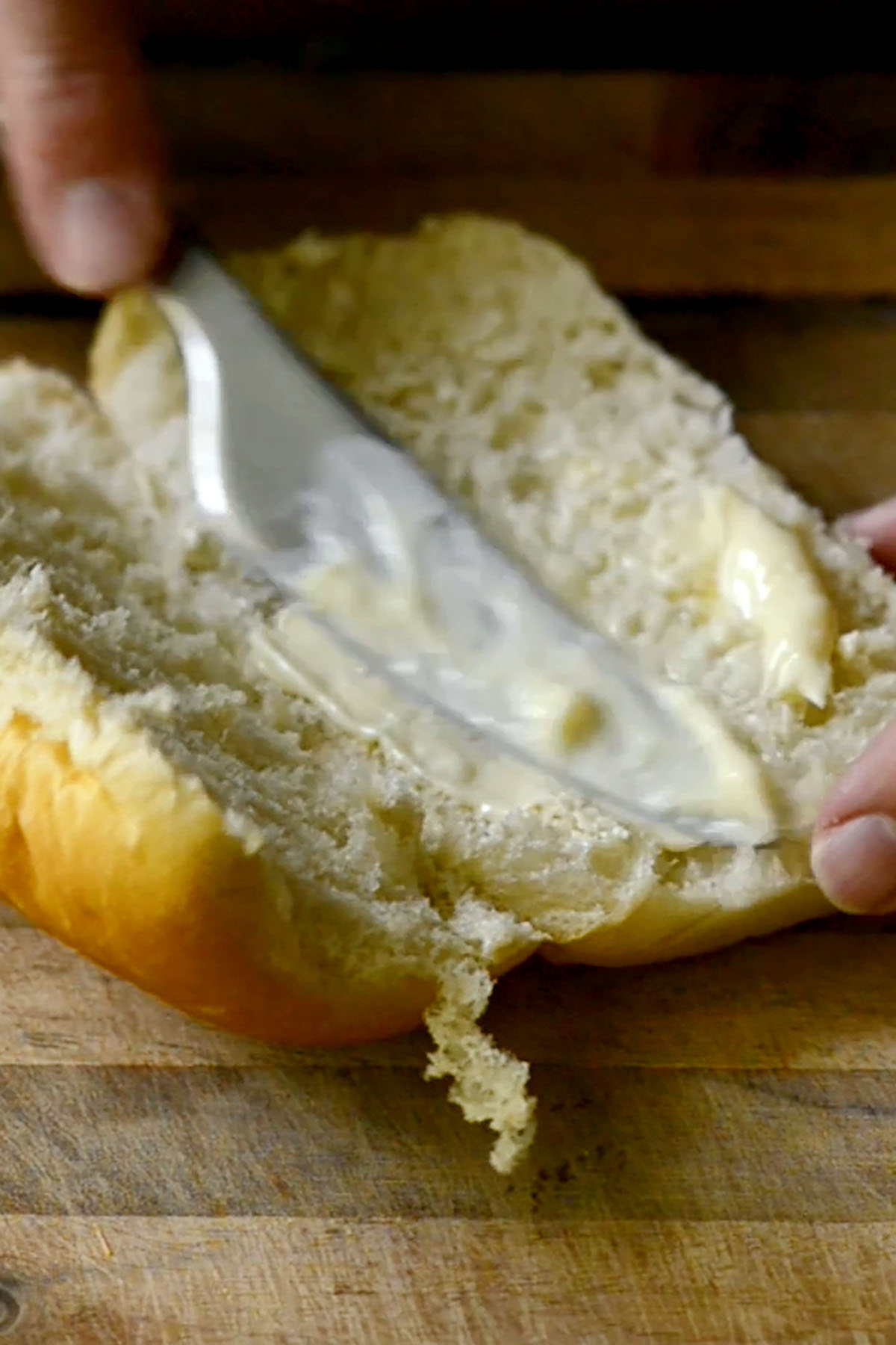 Mayonnaise being spread on a sliced hoagie bun.