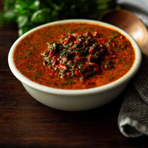 Red chimichurri in a white serving bowl on a wooden table.