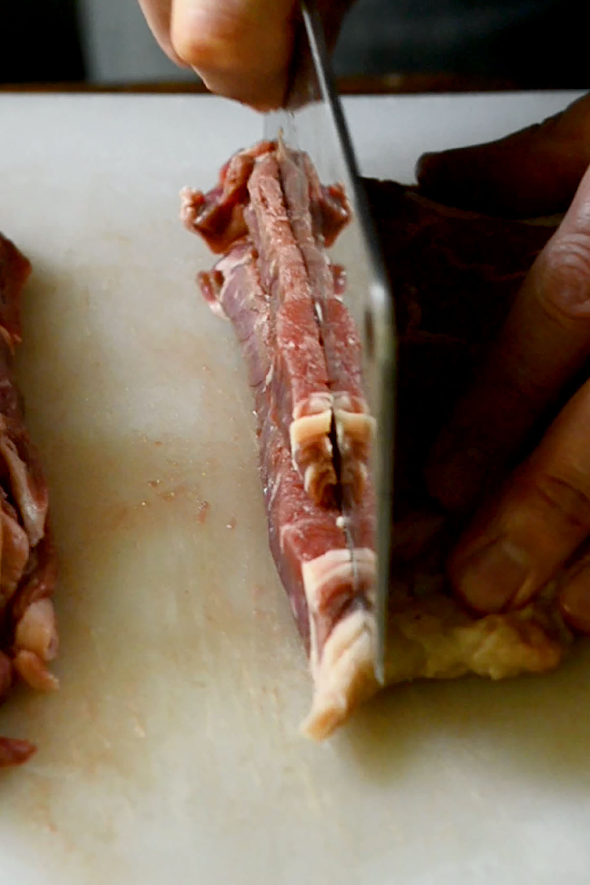 Ribeye steak being thinly slice with a butcher knife.