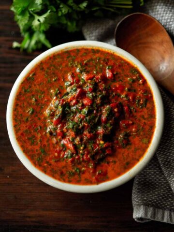 A bowl of red chimichurri sauce served with a wooden spoon on the side.