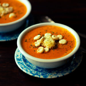 Roasted Red Pepper Gouda Soup topped with shredded gouda cheese, oyster crackers, and fresh parsley.