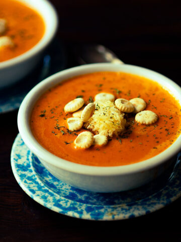 Roasted Red Pepper Gouda Soup topped with shredded gouda cheese, oyster crackers, and fresh parsley.