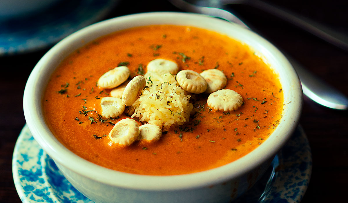 Roasted Red Bell Pepper and Smoked Gouda Soup served with oyster crackers, shredded gouda, and fresh parsley.