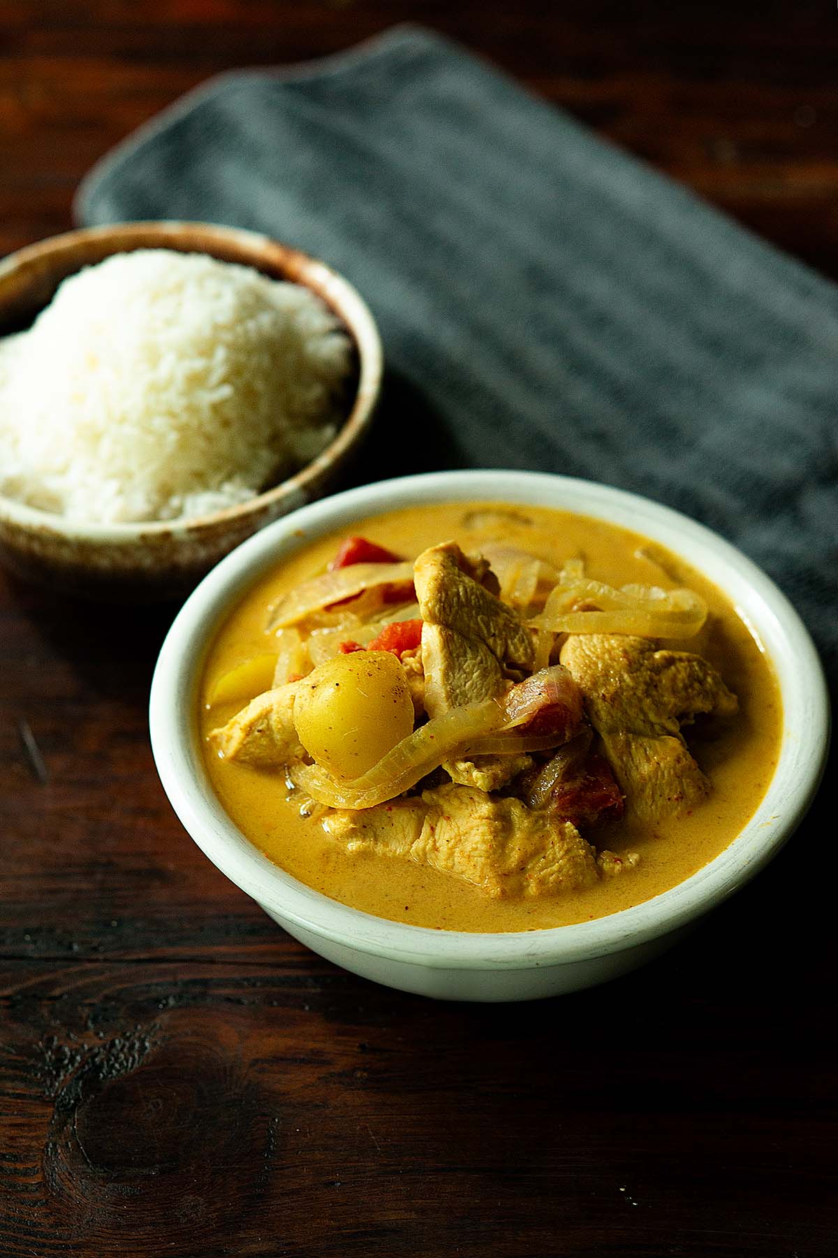 Thai Yellow Curry in a white bowl bowl with a bowl of steamed white rice on the side.