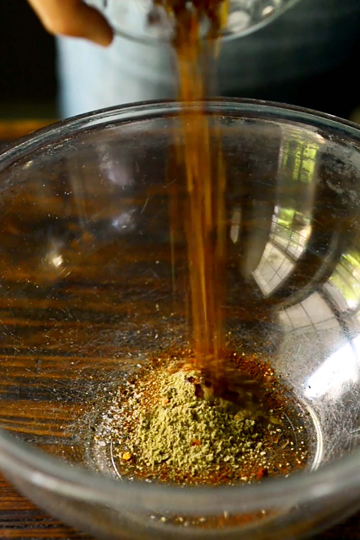 Herbs and spices being poured into a glass mixing bowl.