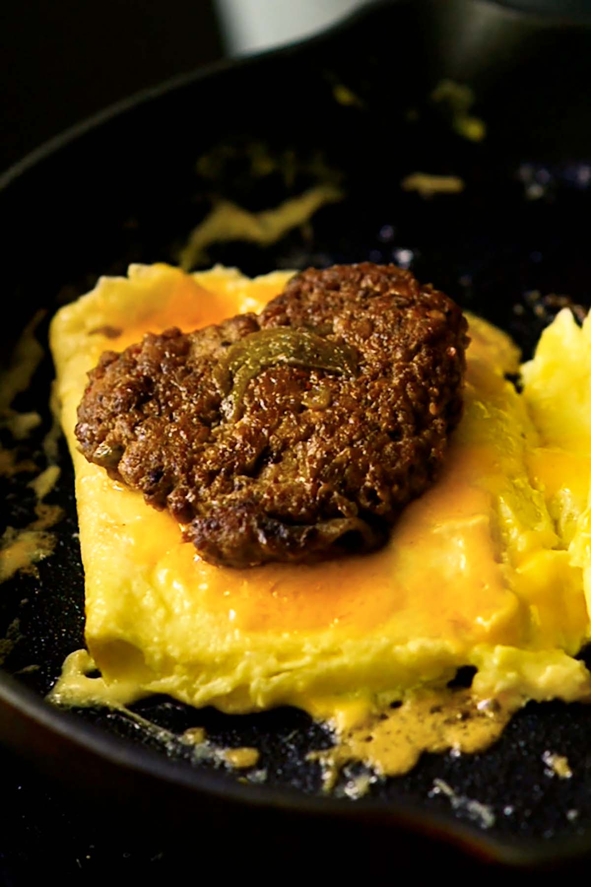 Scrambled eggs folded into a square, topped with cheddar cheese and a hatch chile chicken breakfast sausage patty.