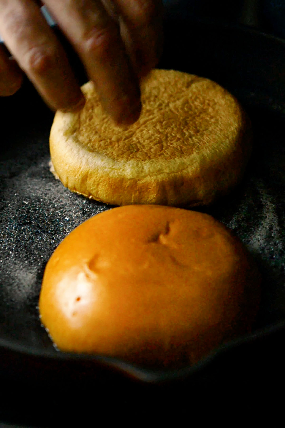 A brioche bun being toasted in a cast iron skillet.